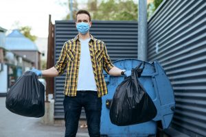 Residential resident in mask holds plastic trash bags
